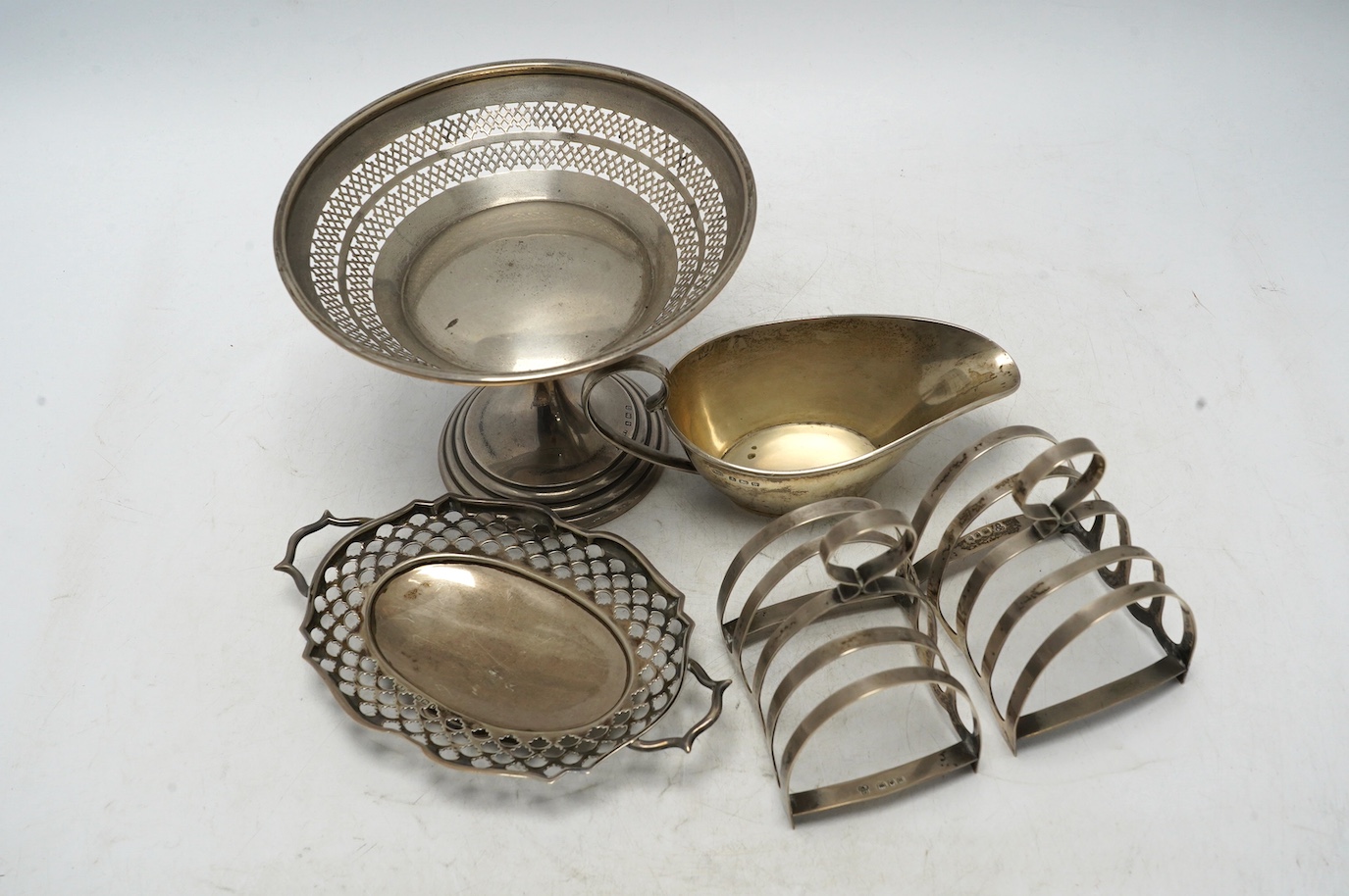 A pair of George VI silver five bar toast racks, Charles Boyton & Sons Ltd, London, 1937, 79mm, together with a small silver sauce boat, a silver two handled shallow dish and a pierced silver tazze, 15oz. Condition - fai